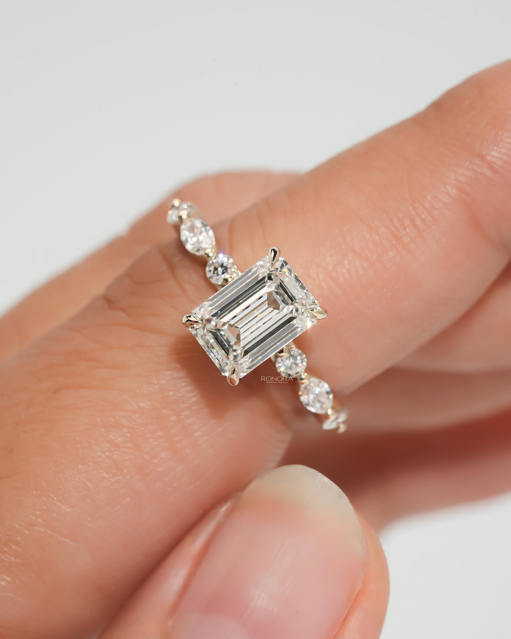 Emerald cut lab grown diamond ring in yellow gold with round and marquise side diamonds, held between fingertips