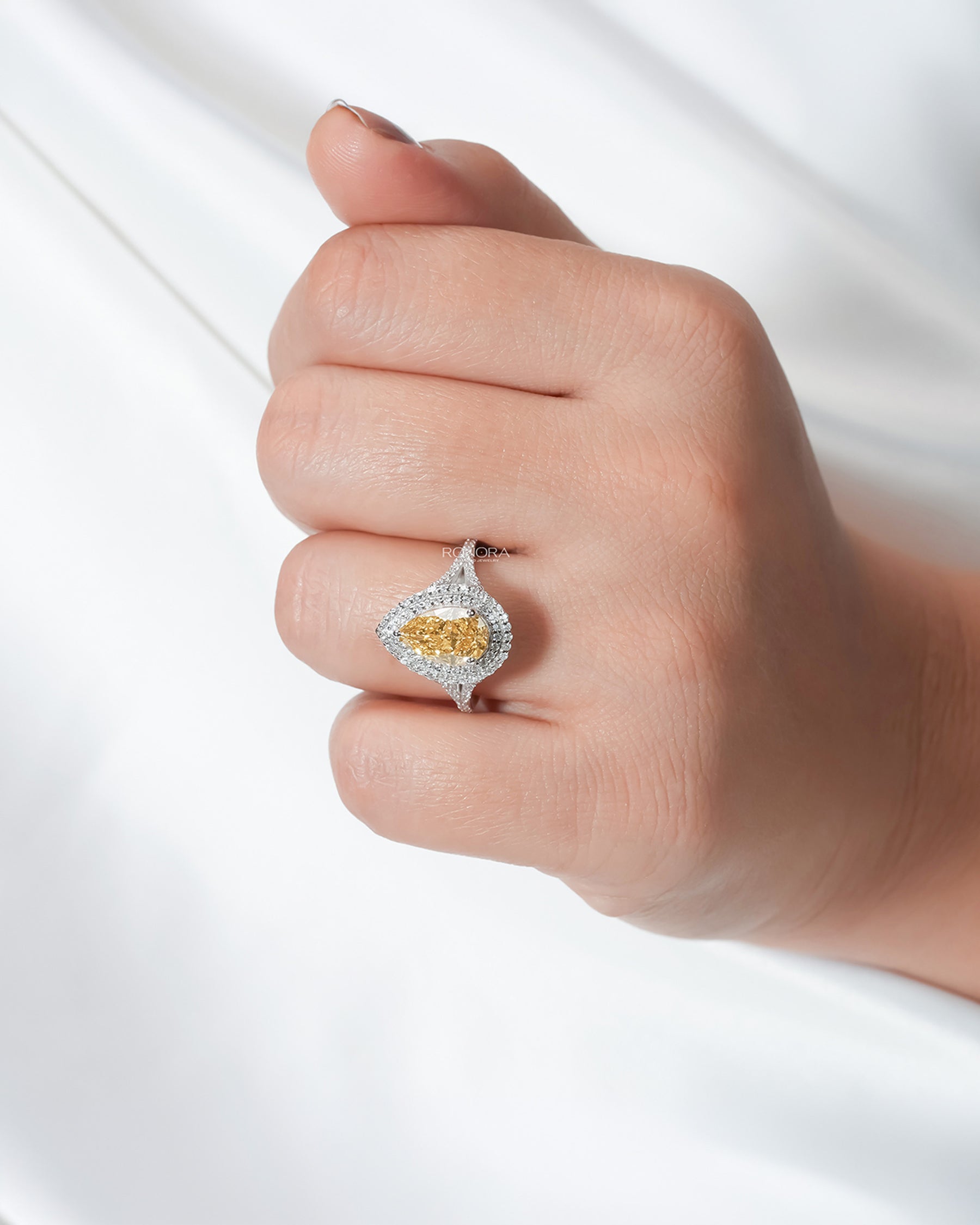 Yellow pear lab grown diamond halo ring worn on hand in white metal