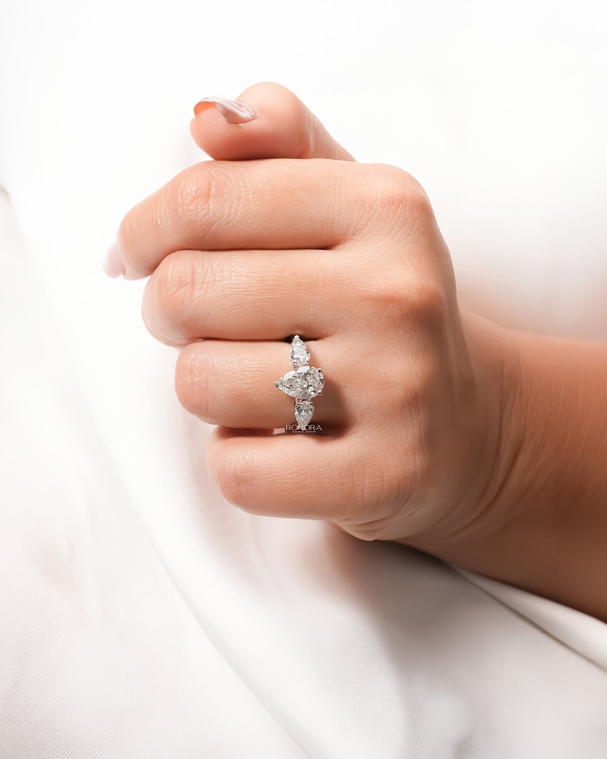 Pear lab grown diamond three-stone ring worn on hand in white metal