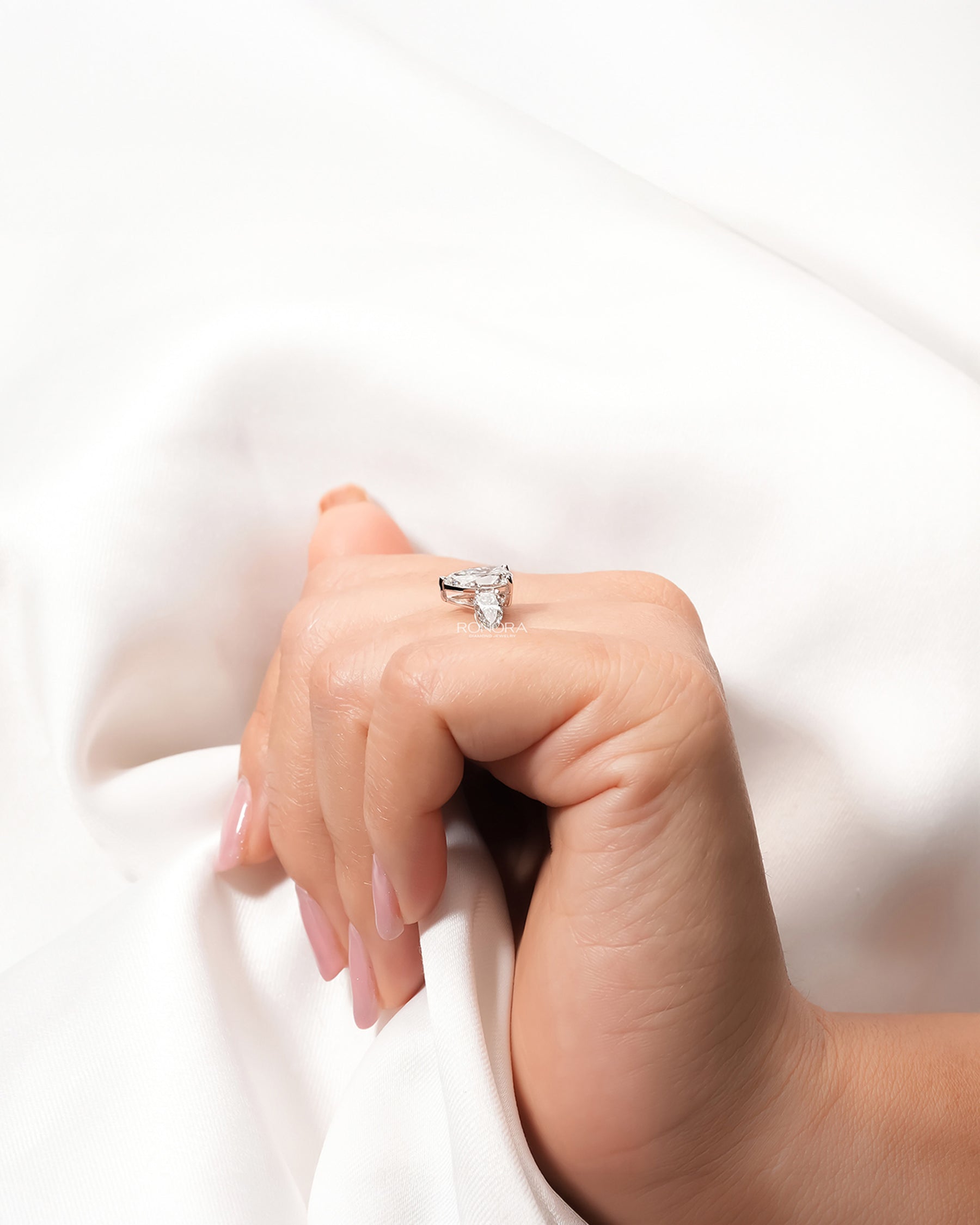 Pear lab grown diamond three-stone ring worn with white silk
