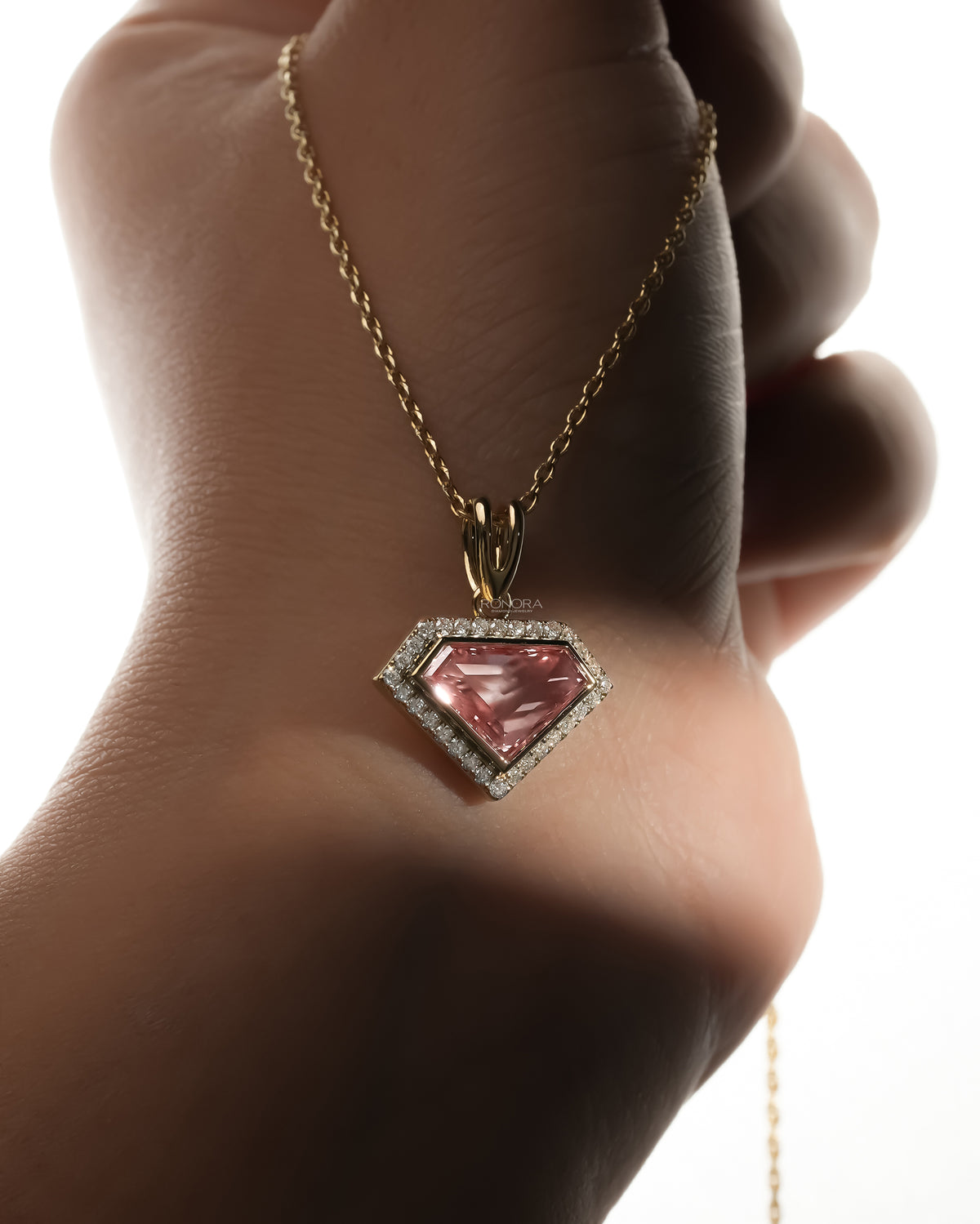Pink shield cut lab grown diamond necklace in yellow gold hanging over a hand, backlit close-up of the halo