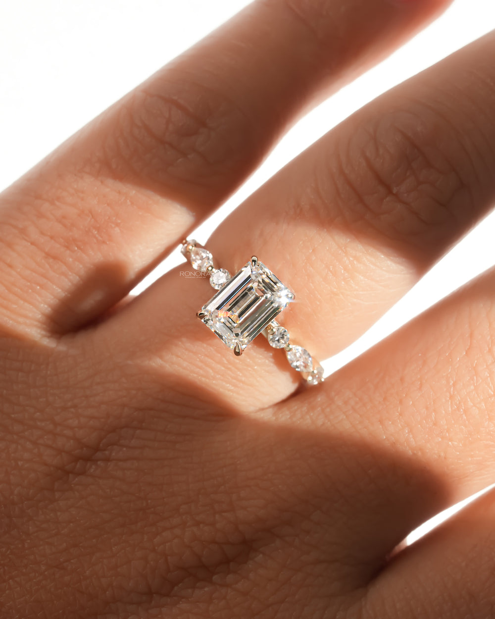 Emerald cut lab grown diamond ring in yellow gold with marquise and round side diamonds, worn on a hand in sunlight