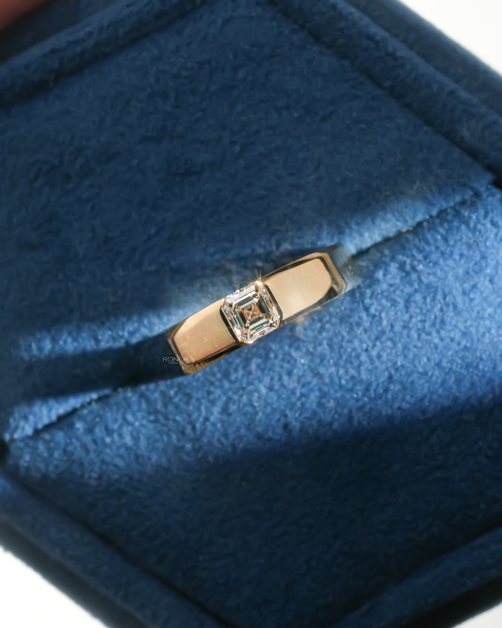 Asscher cut lab grown diamond ring in a wide yellow gold band with bezel setting, resting in a blue velvet ring box