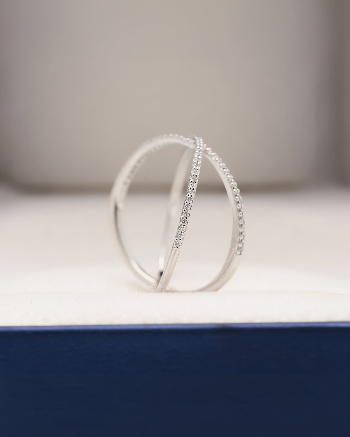 Side profile of white metal pavé crossover ring showing open curved bands