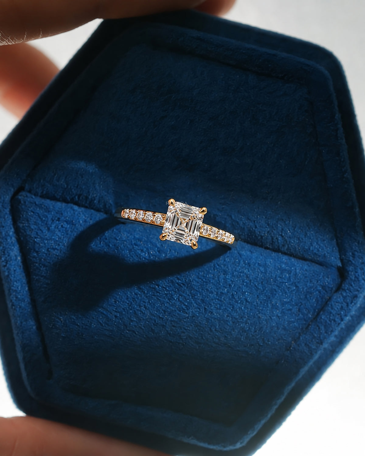 Asscher cut pave lab grown diamond ring in yellow gold, resting in a blue velvet ring box held in hand