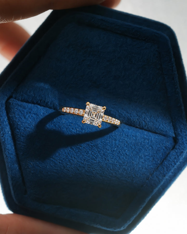 Asscher cut pave lab grown diamond ring in yellow gold, resting in a blue velvet ring box held in hand