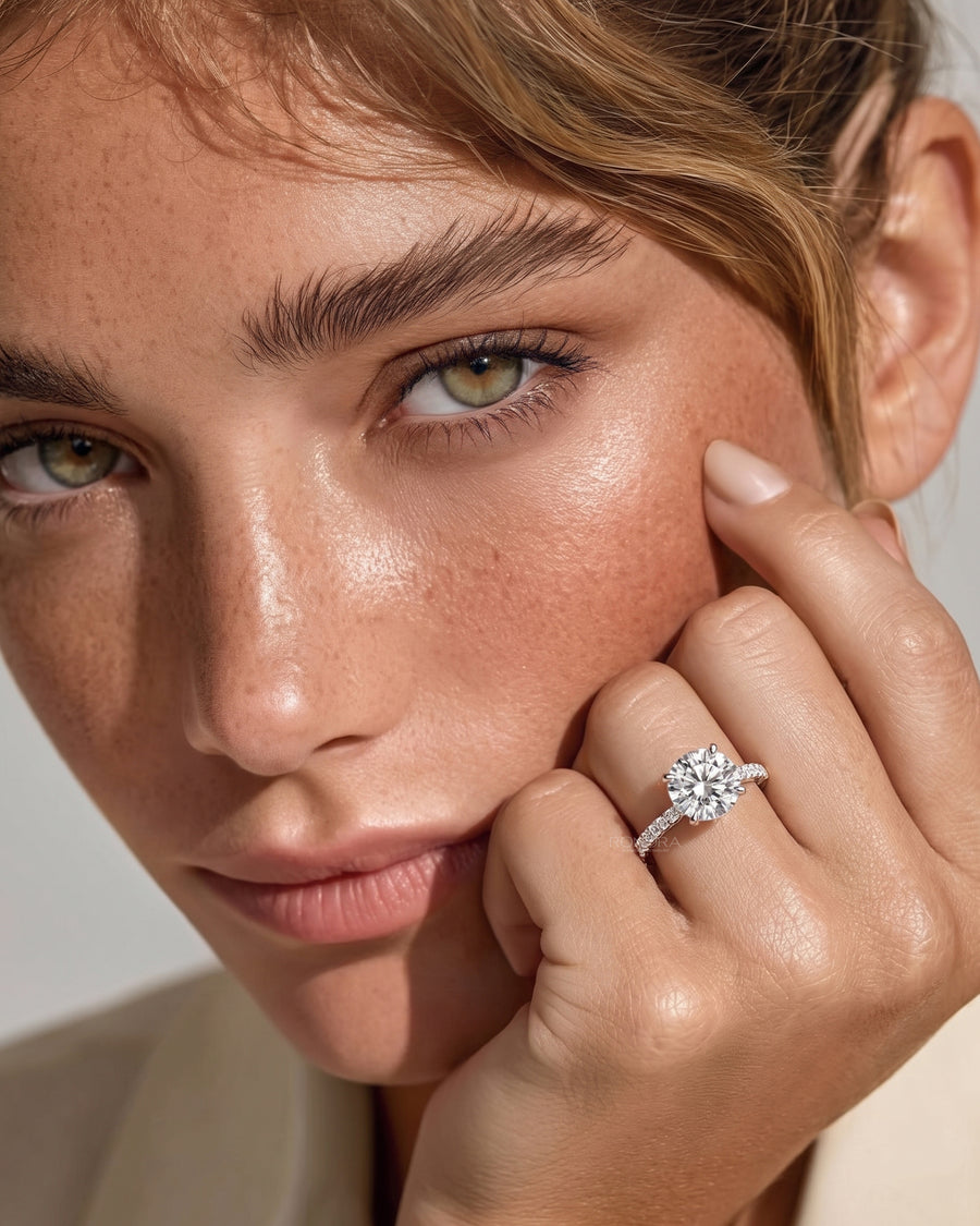 Model resting her hand on her cheek wearing a round hidden halo lab grown diamond ring with a pave band