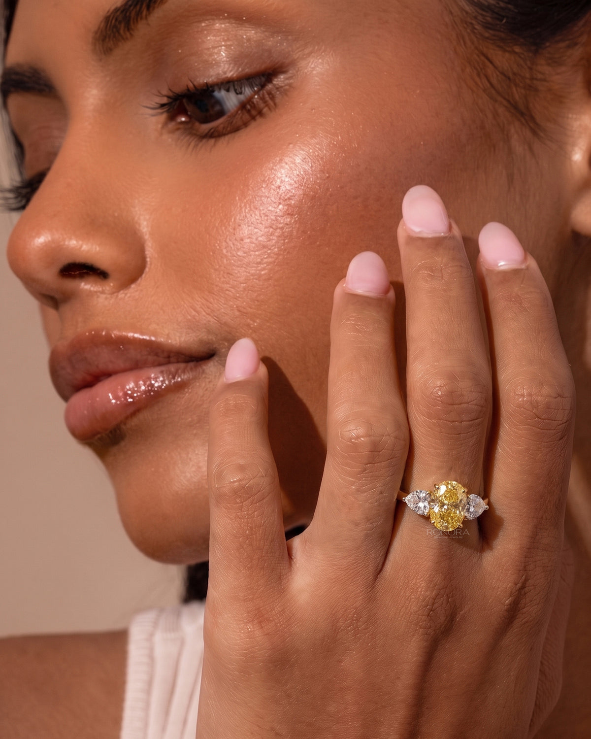 Model touching her cheek wearing an oval yellow lab grown diamond ring with white heart shaped side stones