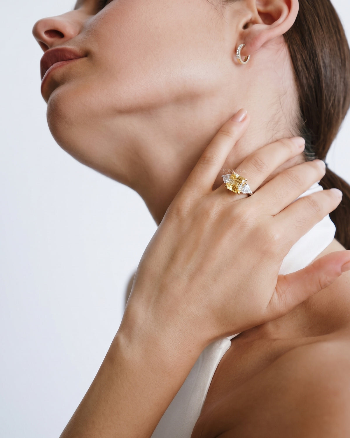 Model with her hand at her neck wearing an asscher yellow lab grown diamond ring with white side stones