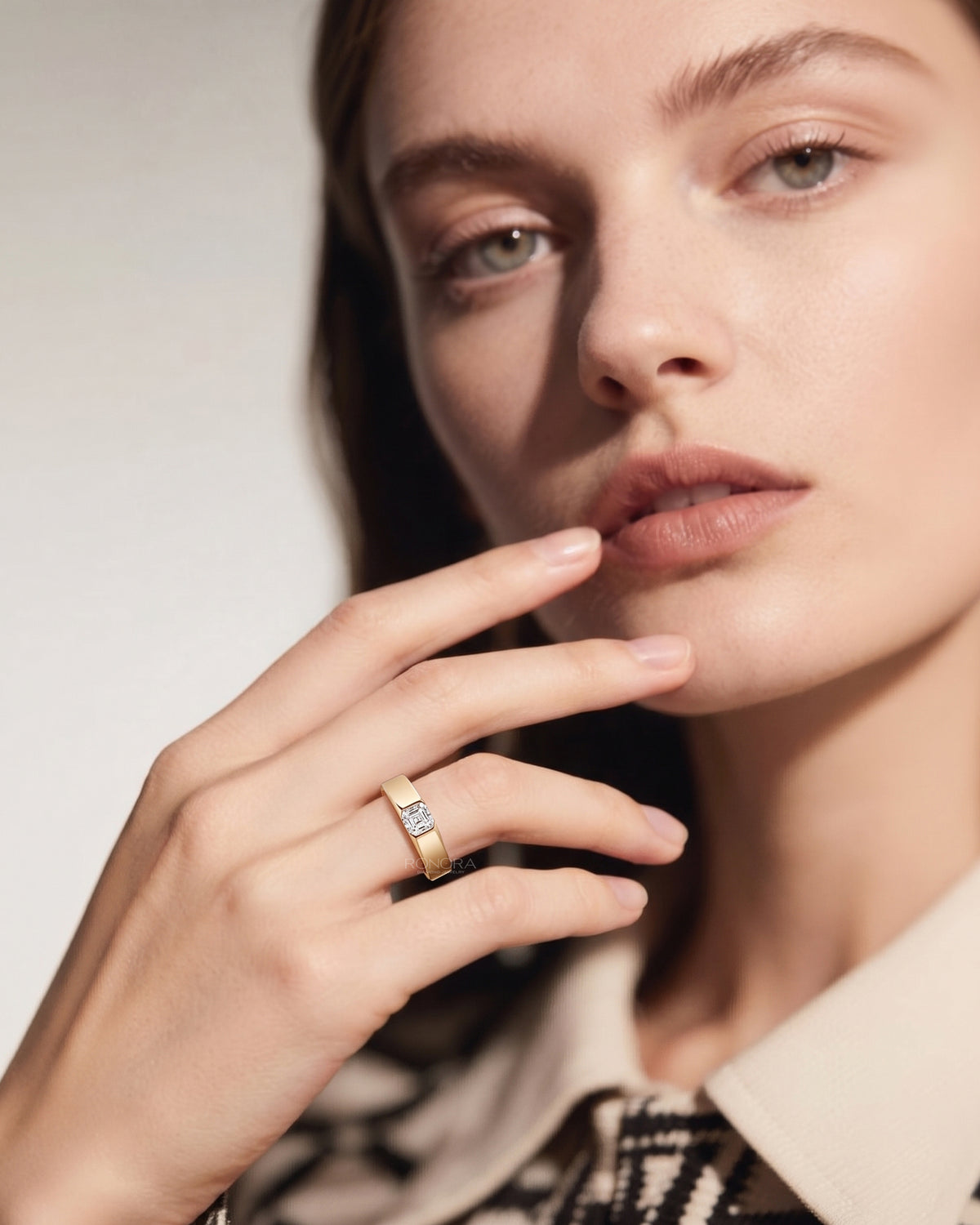 Woman with her hand near her lips wearing an asscher cut lab grown diamond ring in a wide yellow gold band
