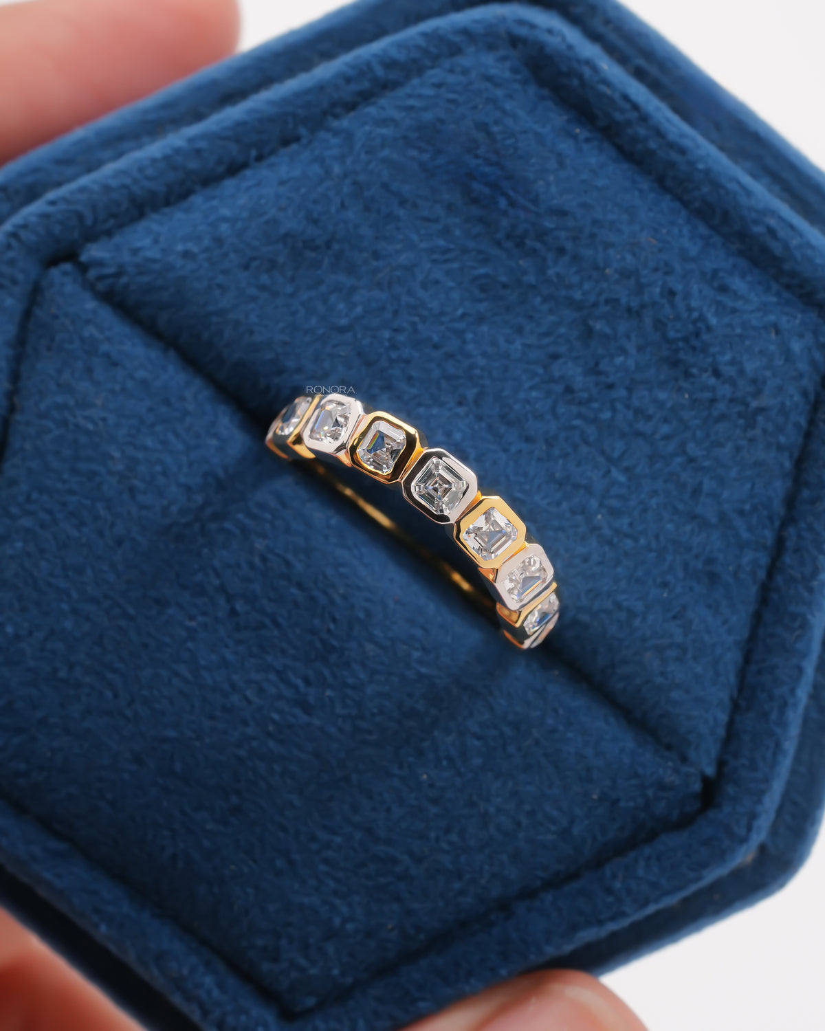 Top view of an asscher cut lab grown diamond eternity band with bezel set stones resting in a blue velvet ring box