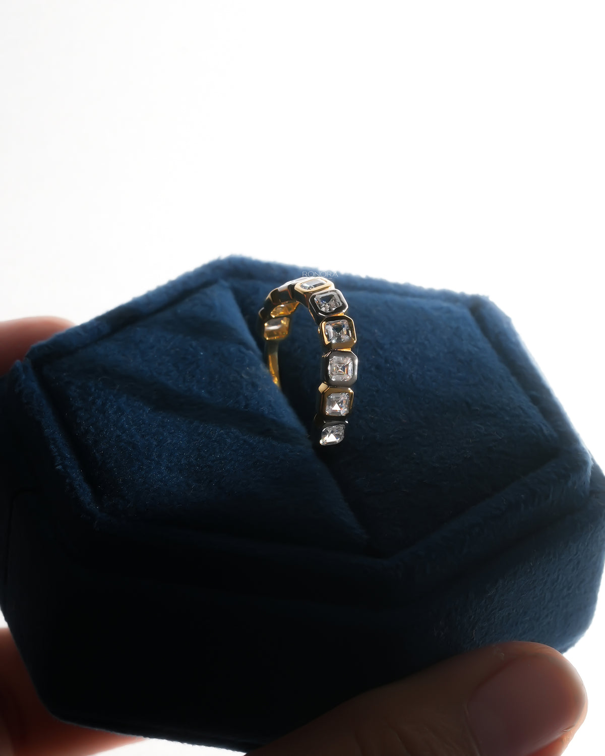 Bezel set asscher cut lab grown diamond eternity band standing upright in a navy velvet ring box held in hand