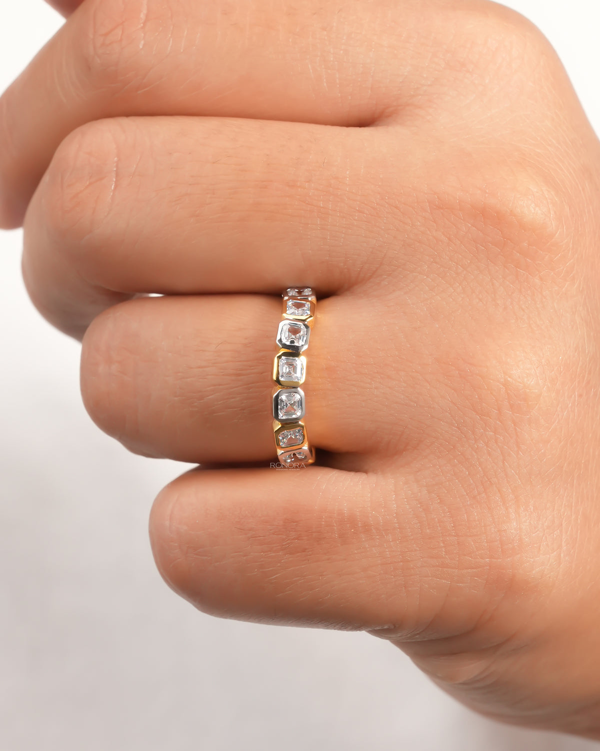 Asscher cut lab grown diamond eternity band on a finger with alternating yellow and white gold bezels, front view