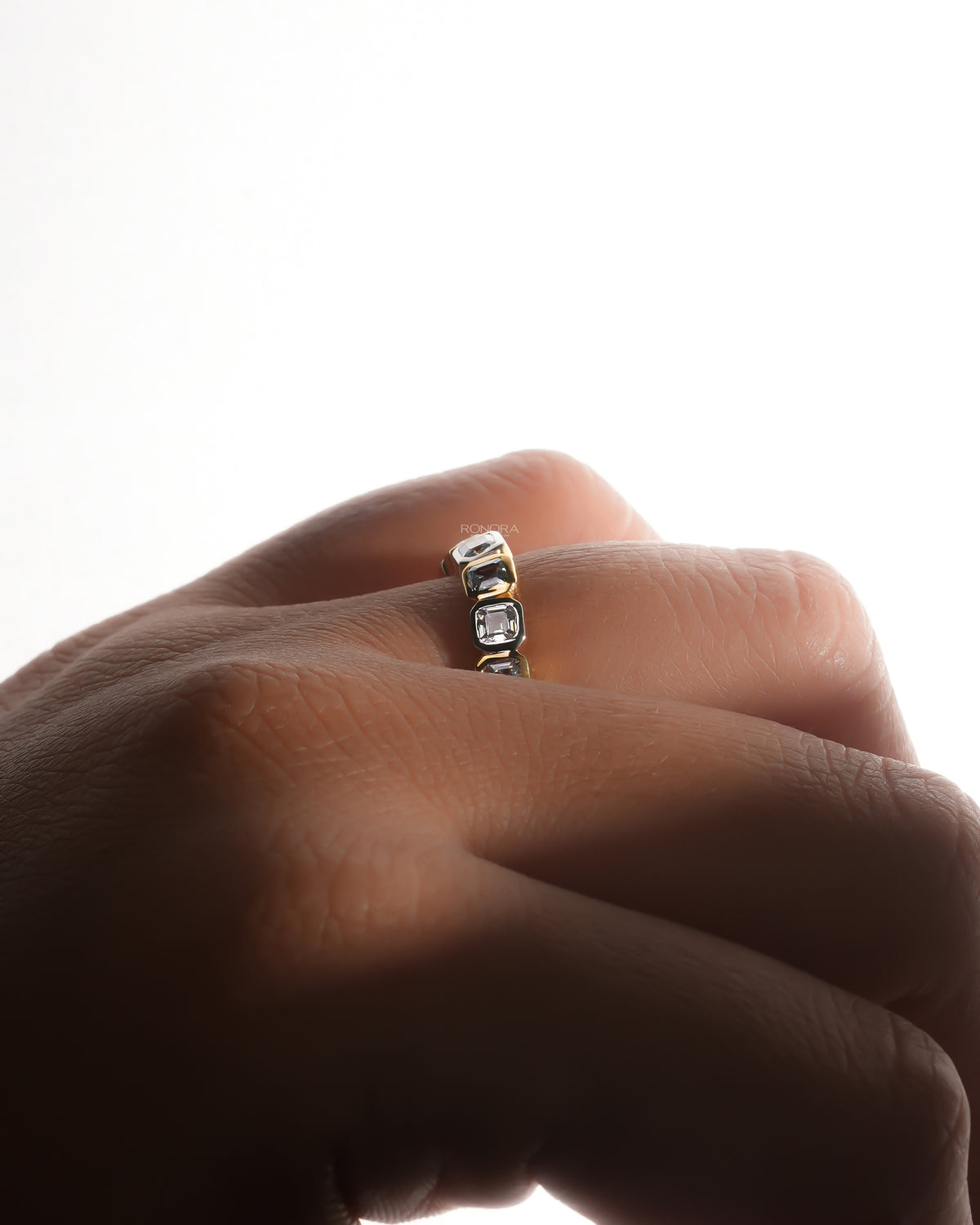 Asscher cut lab grown diamond eternity band with bezel set stones in alternating gold tones, worn on a backlit hand