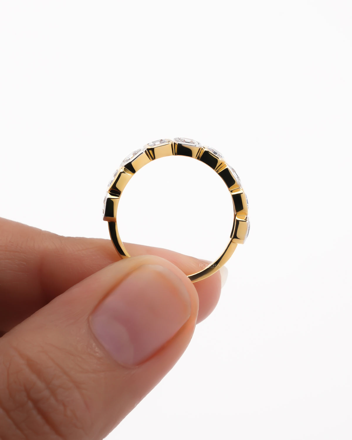 Yellow gold asscher cut lab grown diamond eternity band held upright between two fingers showing the bezel set profile