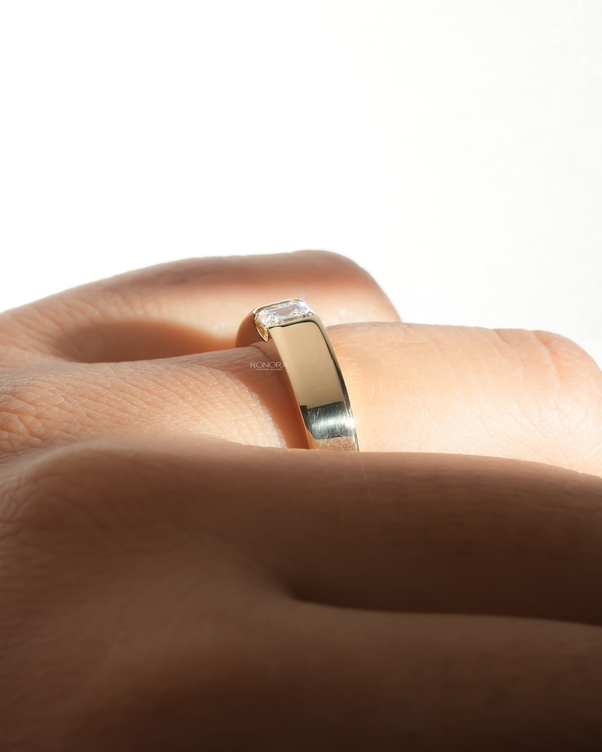 Side view of an asscher cut lab grown diamond ring on a hand, showing the wide polished yellow gold band and bezel setting