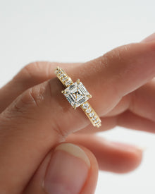 Close-up of an asscher cut pave lab grown diamond ring in yellow gold held between fingers