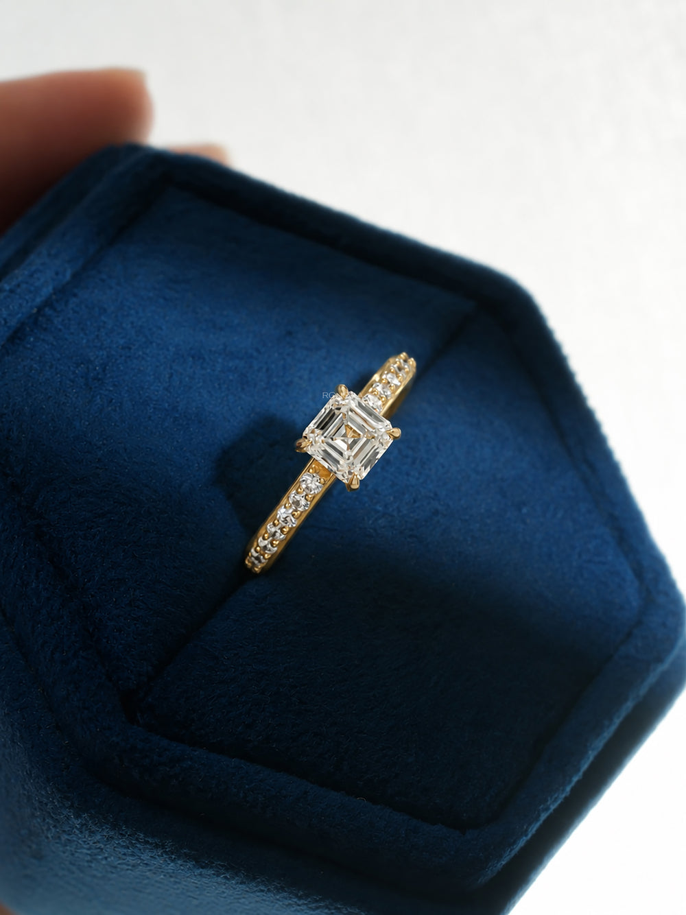 Asscher cut pave lab grown diamond ring in yellow gold angled in a blue velvet hexagon ring box
