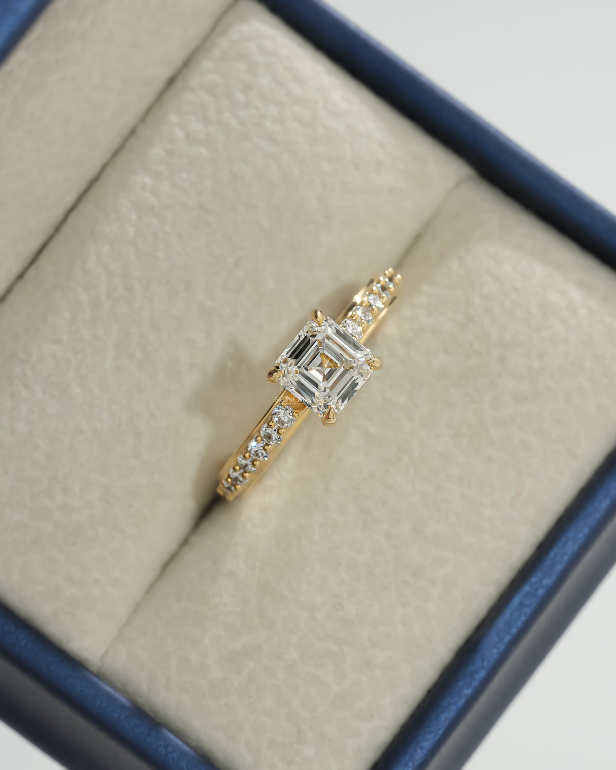 Asscher pave lab grown diamond ring in yellow gold, top view in a cream ring box with a blue rim