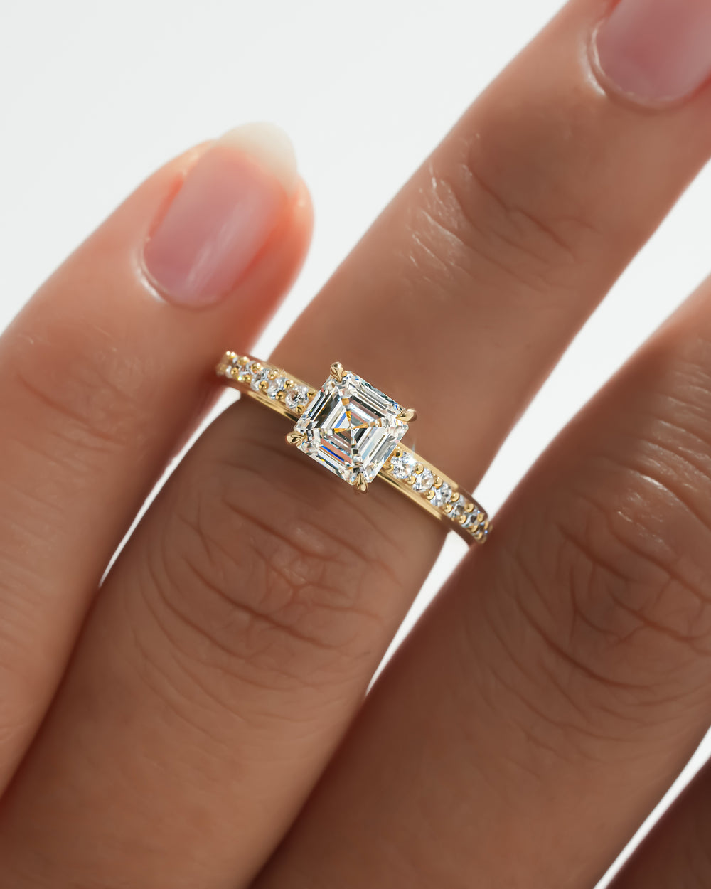 Asscher pave lab grown diamond ring in yellow gold worn on a finger, close-up of the diamond band