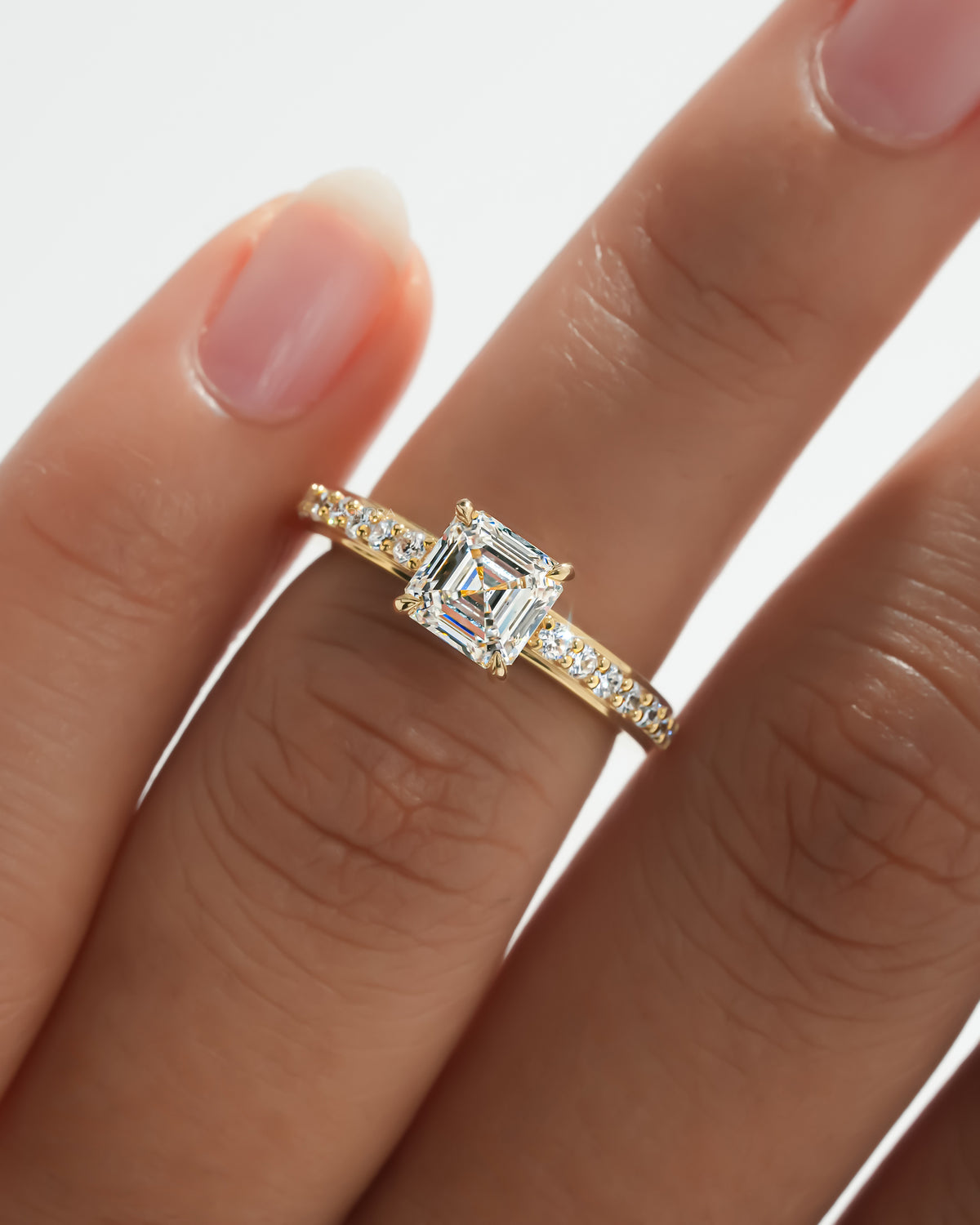 Asscher pave lab grown diamond ring in yellow gold worn on a finger, close-up of the diamond band