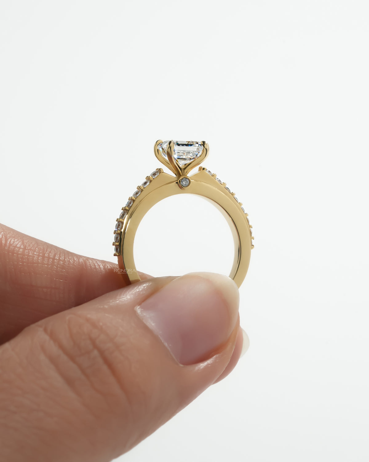 Side profile of an asscher pave lab grown diamond ring in yellow gold, held up to show the hidden diamond