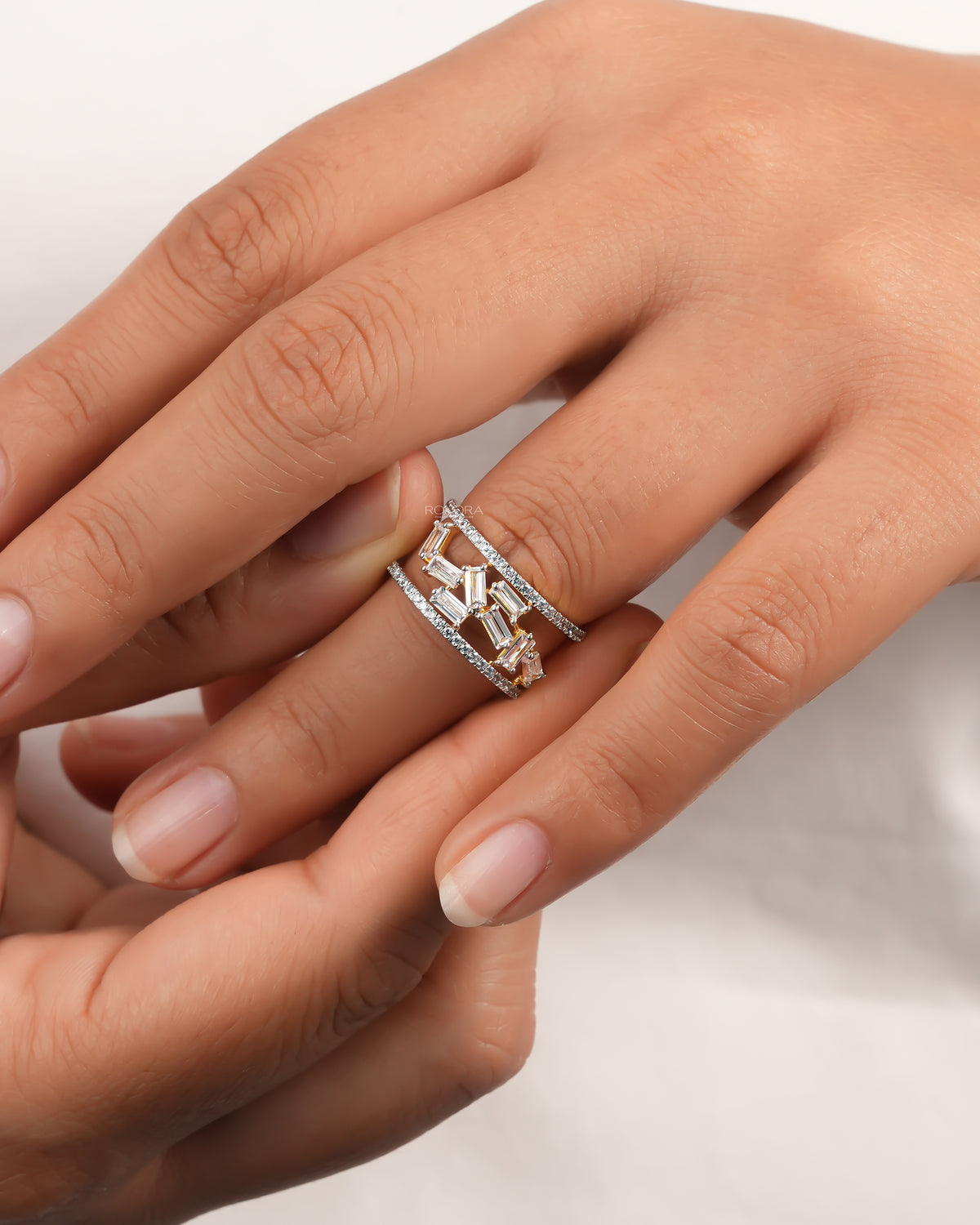 Two hands showing a baguette lab grown diamond cluster ring with scattered baguettes and open pave band