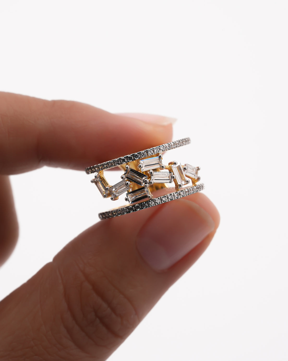 Close-up of a baguette lab grown diamond cluster ring held between fingers, scattered baguettes and two pave rows