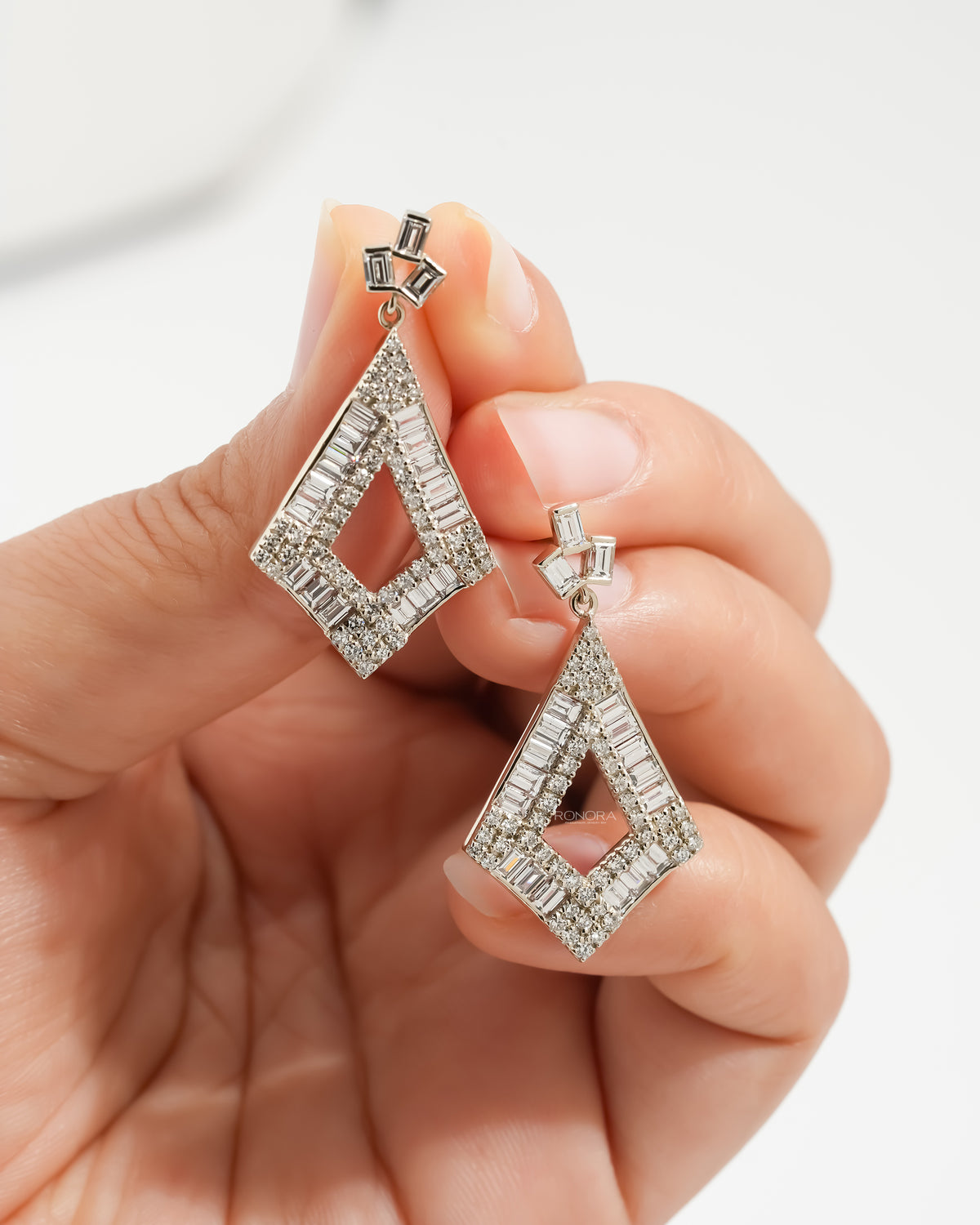 Hand holding a pair of baguette lab grown diamond drop earrings, kite shaped drops with baguette diamond borders