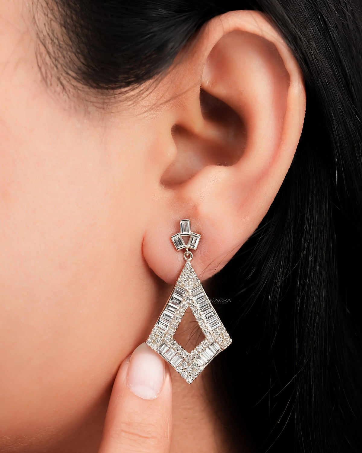 Close-up of a baguette lab grown diamond drop earring worn on the ear, kite shaped drop with baguette diamonds