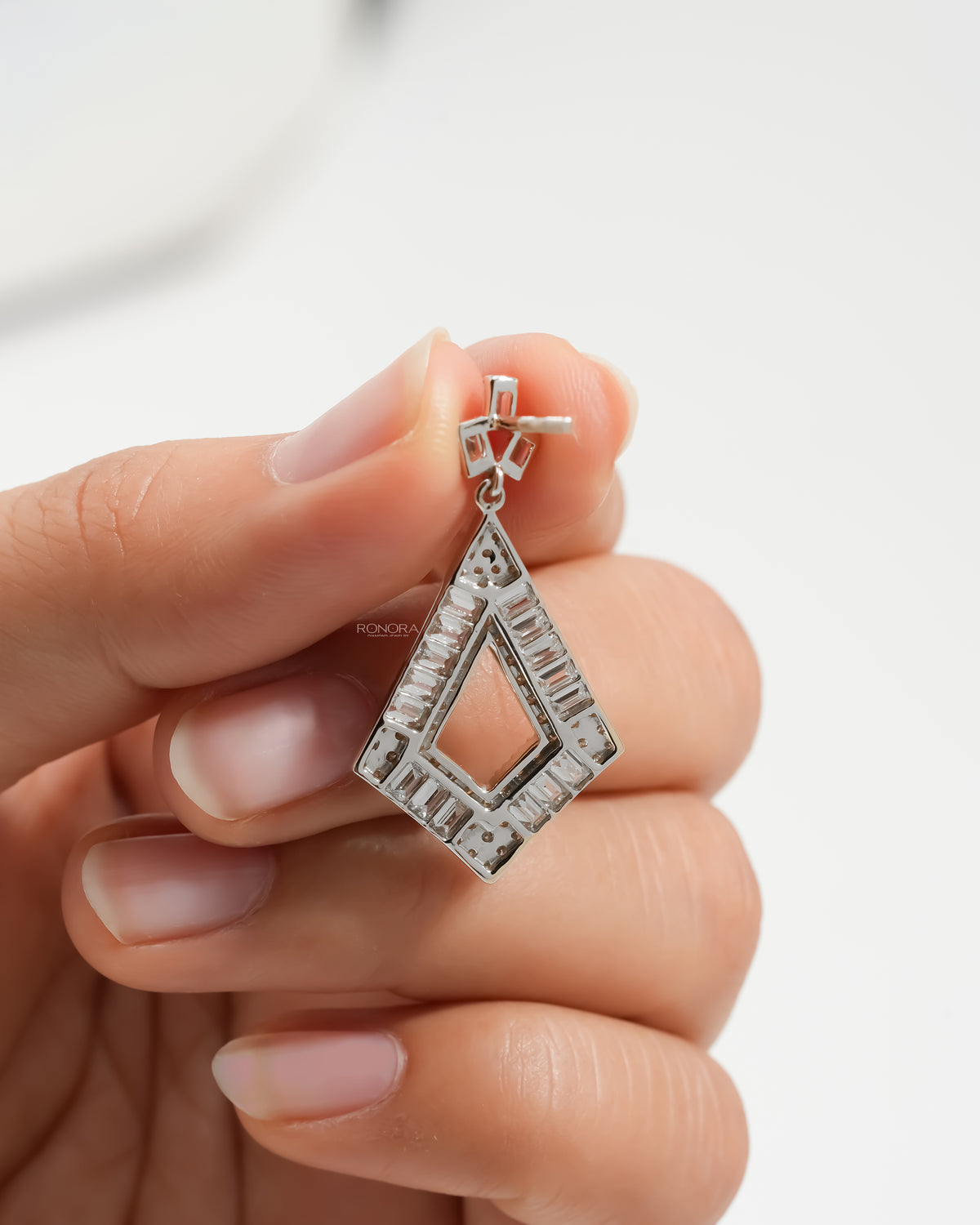 Back view of a baguette lab grown diamond drop earring held in fingers, white gold kite shape with open centre