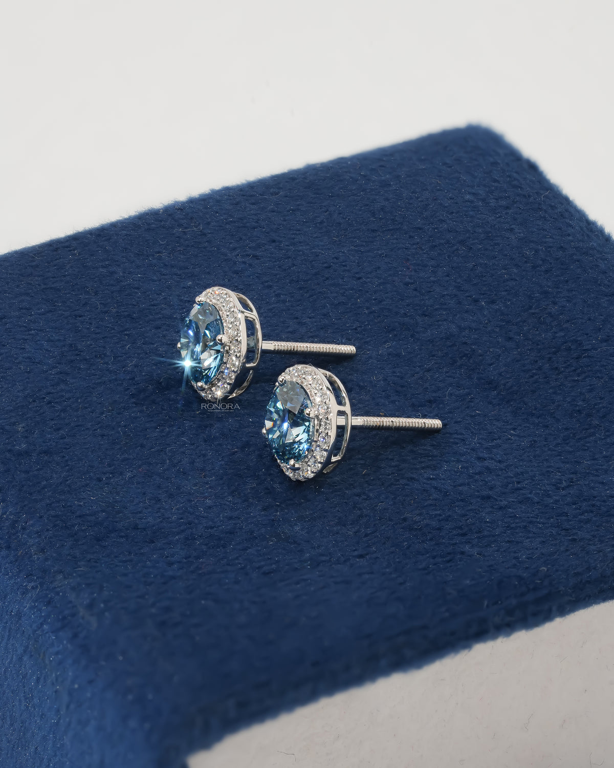 Side view of blue lab grown diamond halo stud earrings in white gold with screw back posts on navy velvet