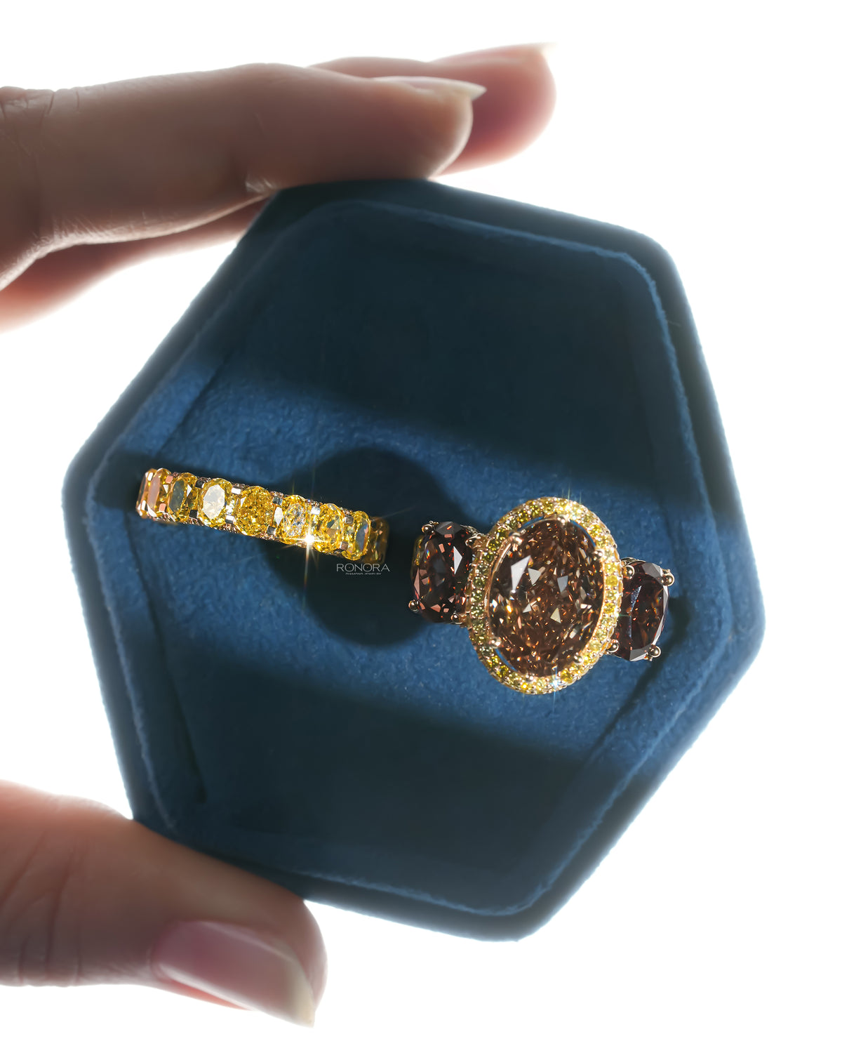 Brown oval lab grown diamond bridal set with halo ring and yellow oval band, resting in a blue velvet hexagon ring box