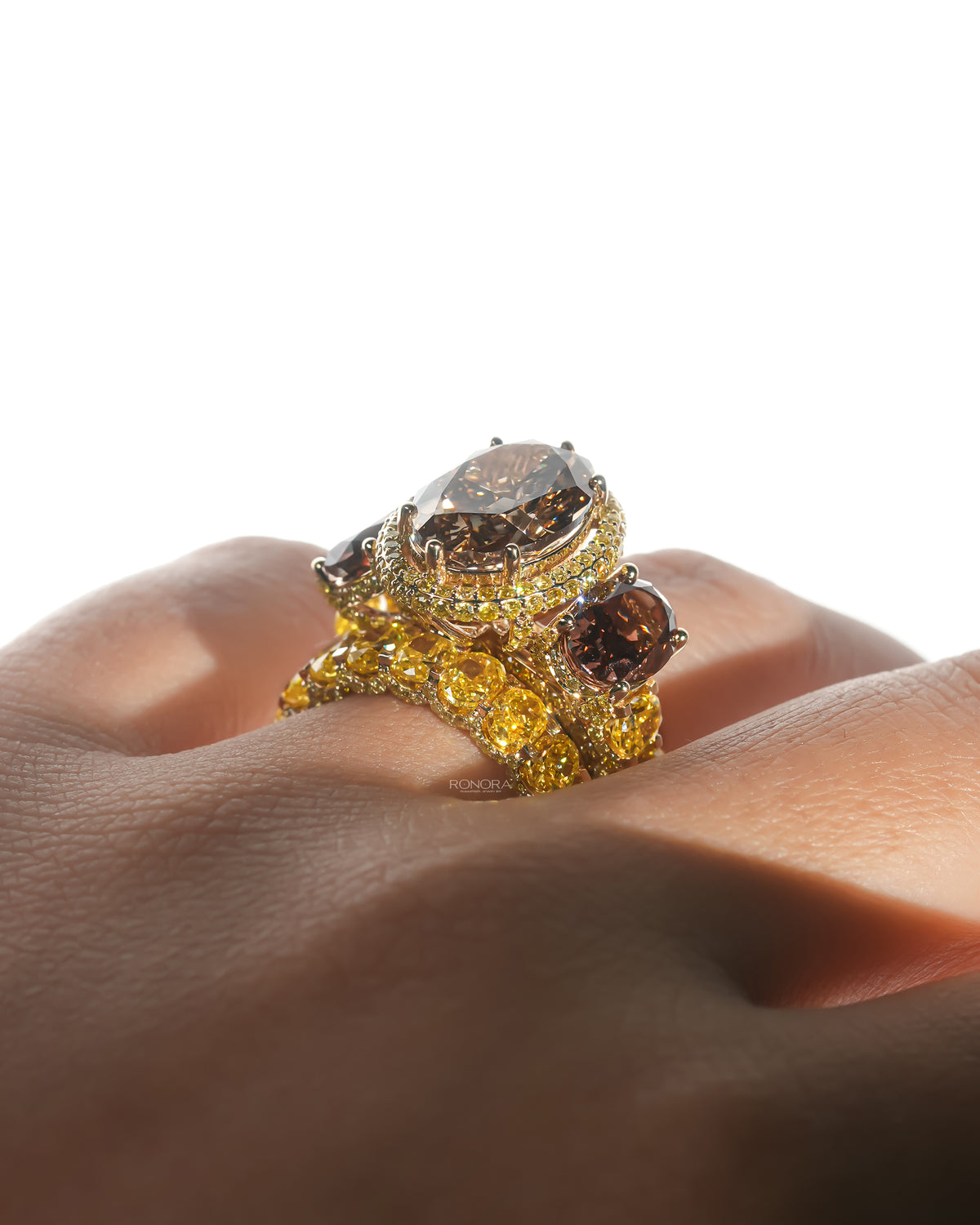 Brown oval lab grown diamond bridal set on a hand, three stone halo ring stacked with a yellow oval stone band