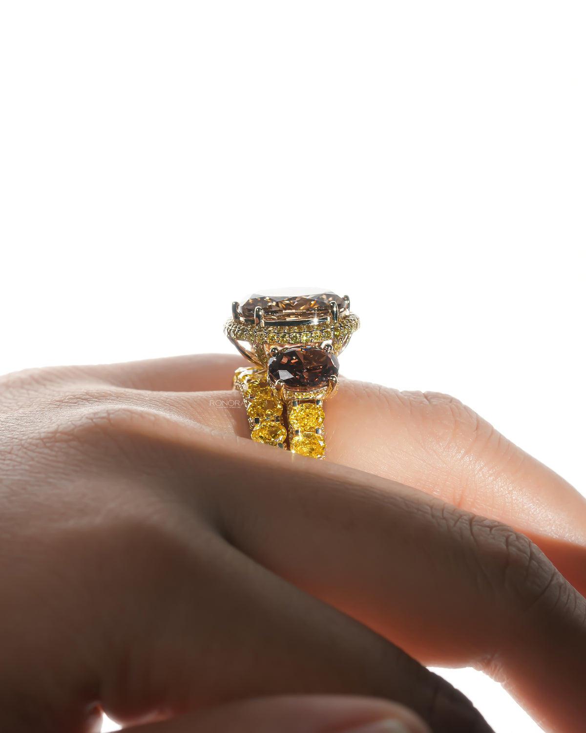 Side profile of a brown oval lab grown diamond bridal set on a finger showing the halo, side stone and yellow oval band