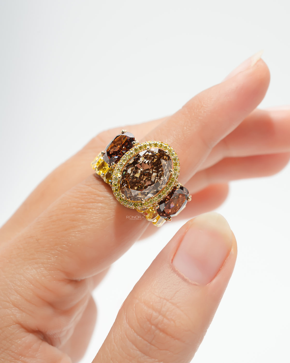 Close-up of a brown oval lab grown diamond bridal set worn on a finger, brown centre stone with yellow halo and side stones