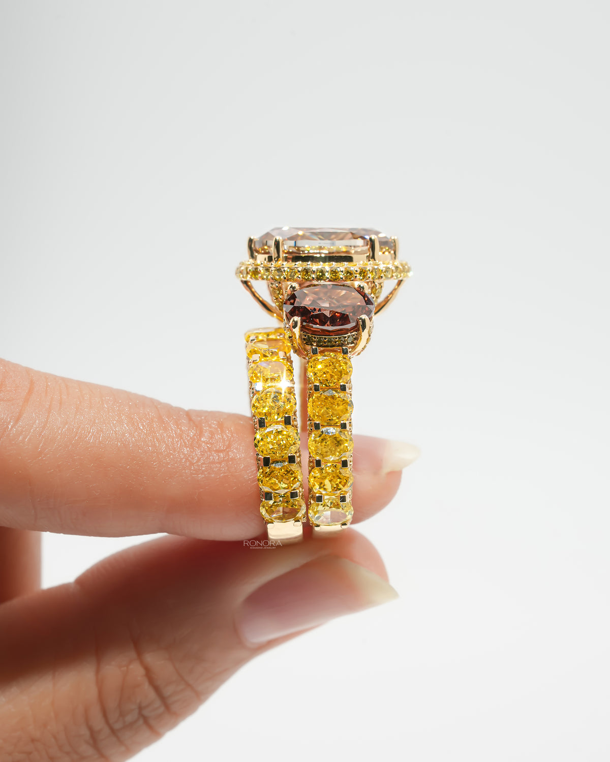 Brown oval lab grown diamond bridal set held between fingers in side view, halo ring beside the yellow oval band