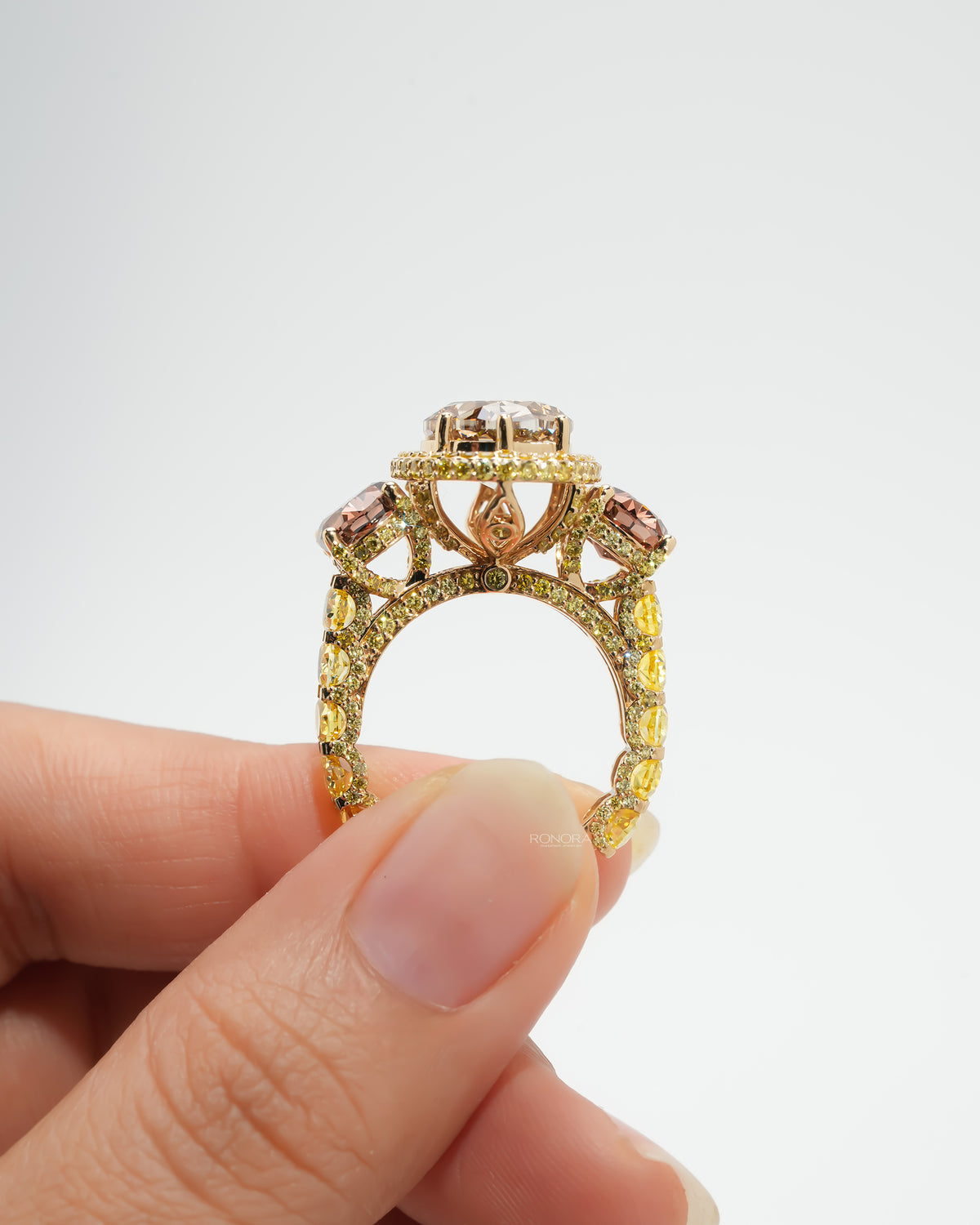 Back view of a brown oval lab grown diamond three stone ring held between fingers, showing the yellow stone band and gallery
