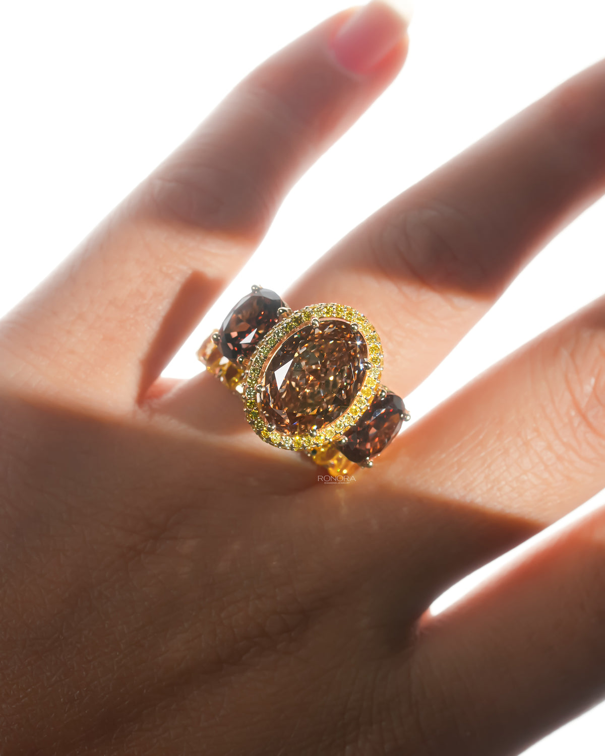 Brown oval lab grown diamond three stone ring worn on a hand in bright backlight, with brown side stones and yellow halo