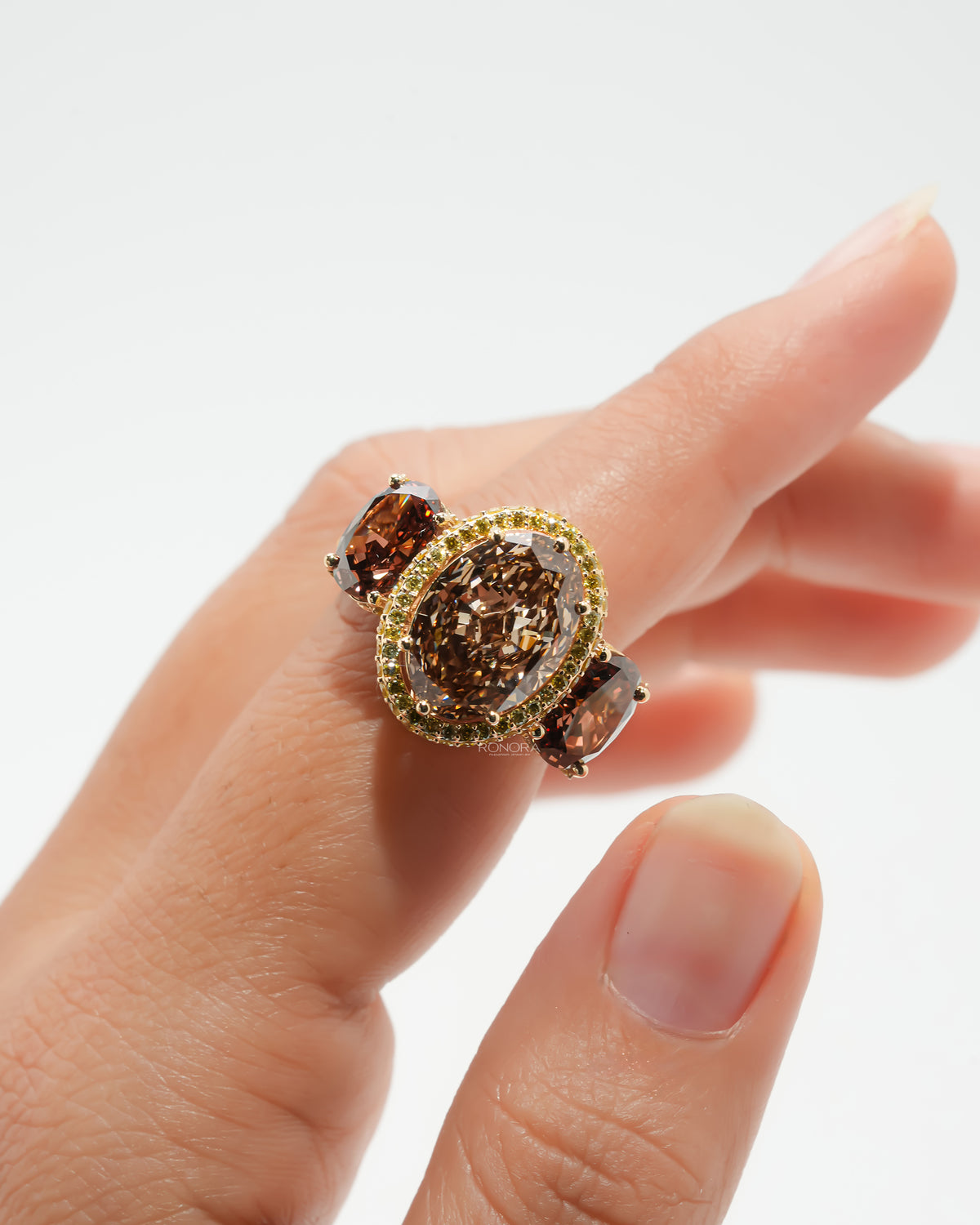 Brown oval lab grown diamond three stone ring with yellow halo worn on a finger, front view with brown side stones