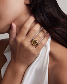 Model's hand at her neck wearing a brown oval lab grown diamond three stone ring with a yellow stone halo