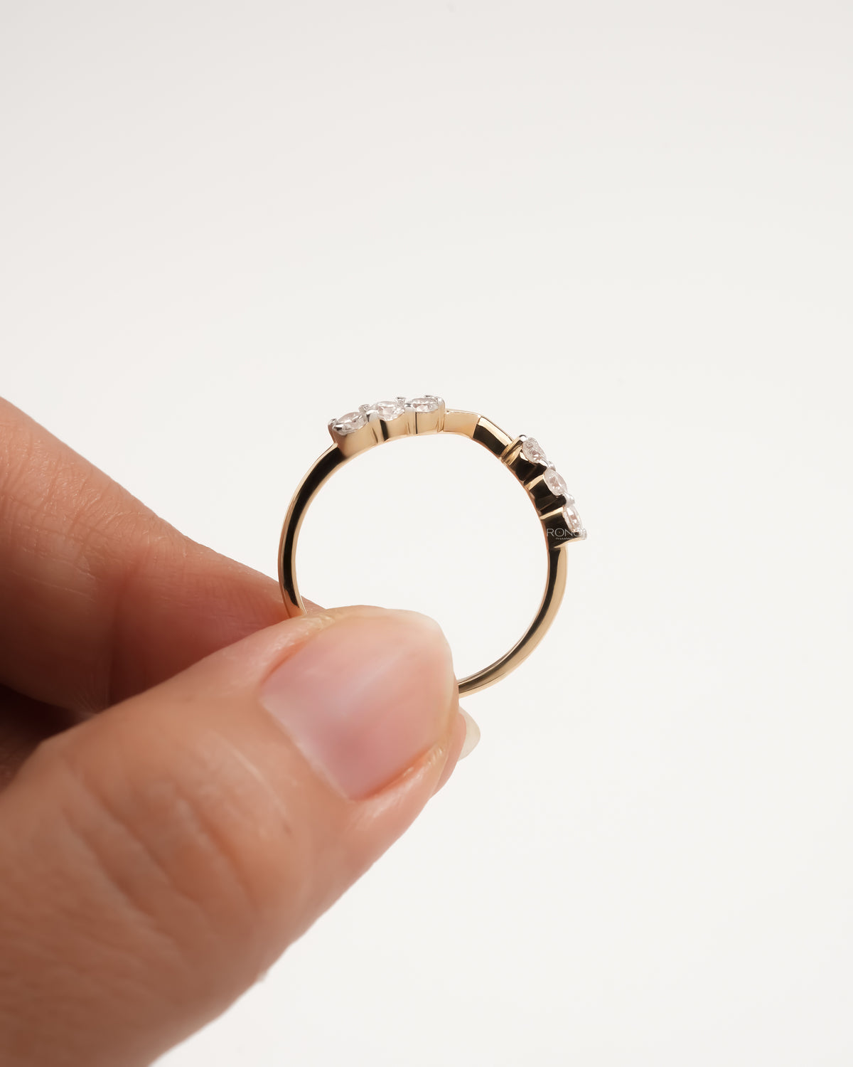 Chevron lab grown diamond wedding band held between thumb and finger, side view of the round stones and band
