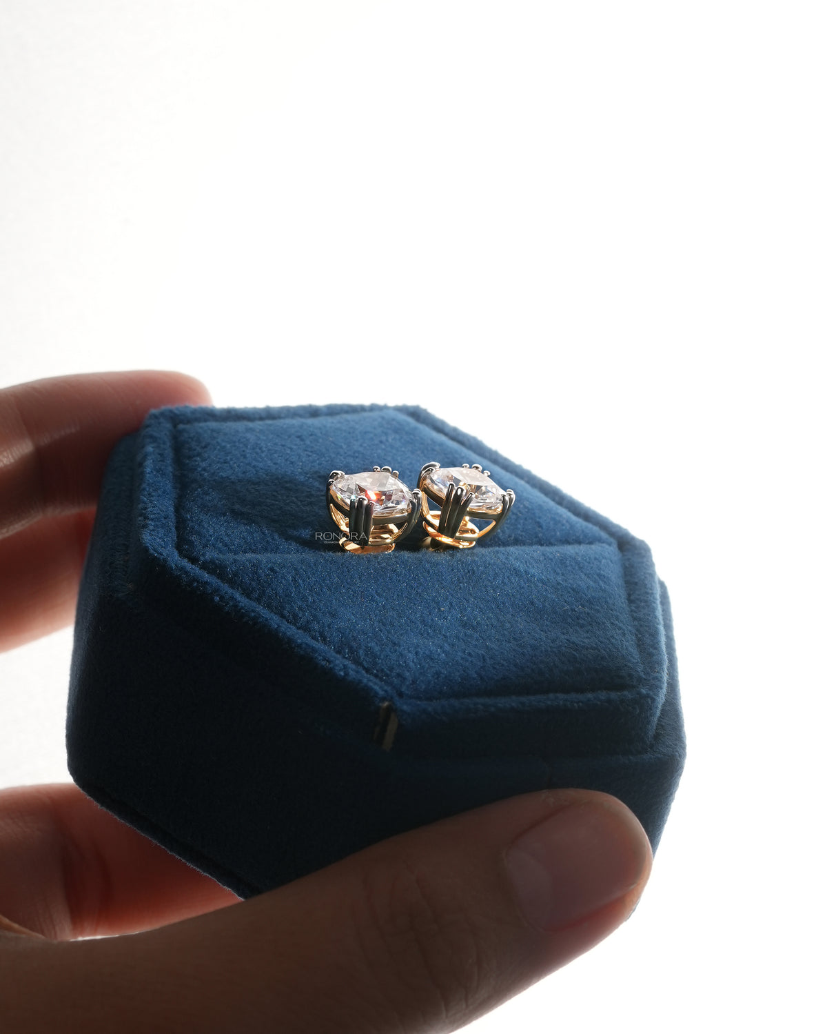 Cushion cut lab grown diamond earrings in a blue velvet jewelry box held between fingers