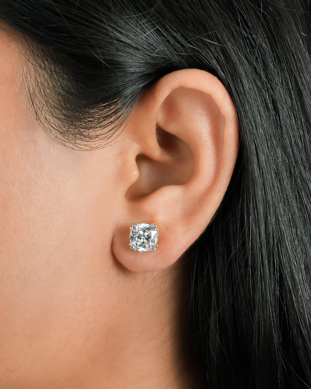 Cushion cut lab grown diamond stud earring worn on a woman's ear, close-up of the prong setting