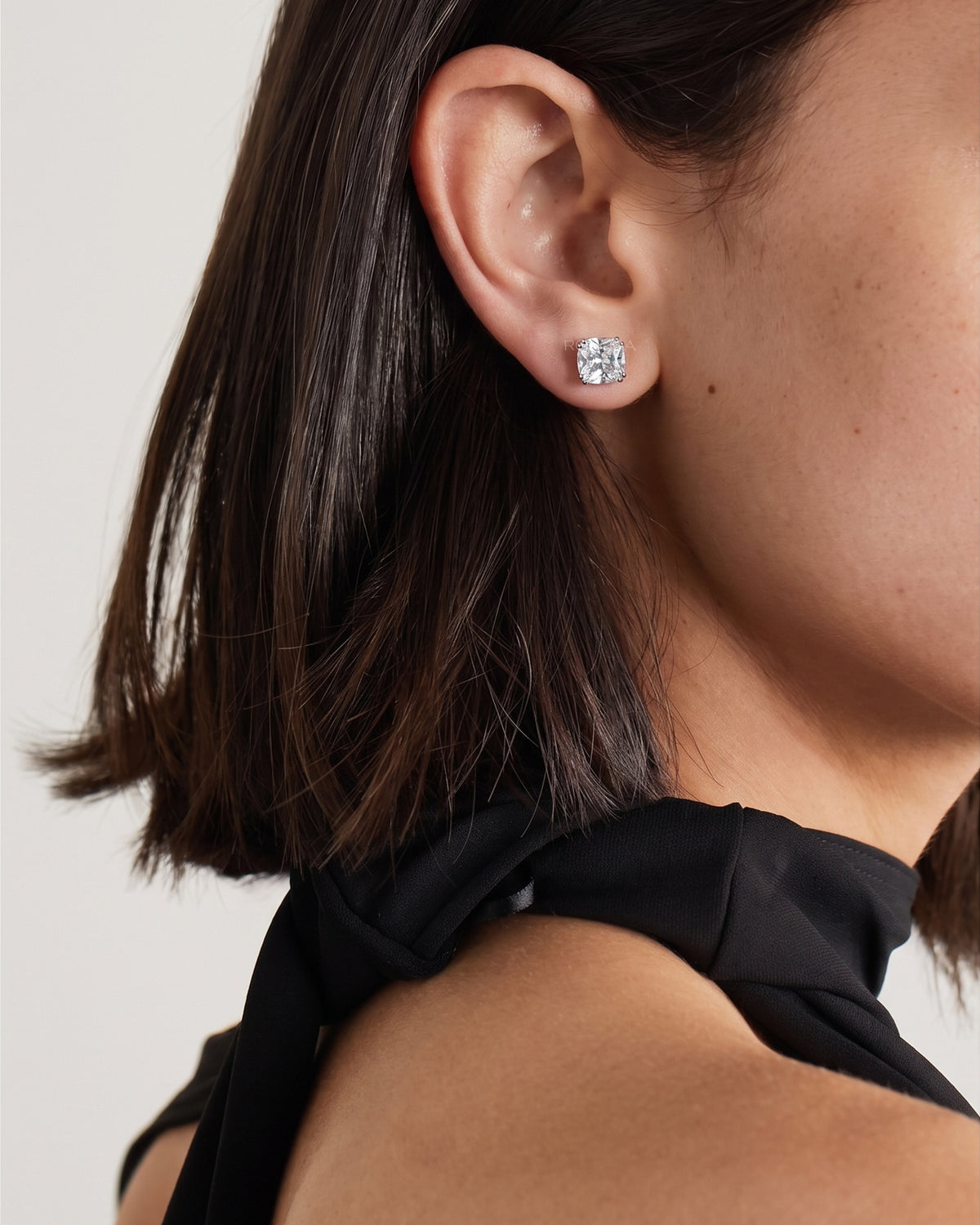 Model wearing a cushion cut lab grown diamond stud earring, side profile close-up with a black top