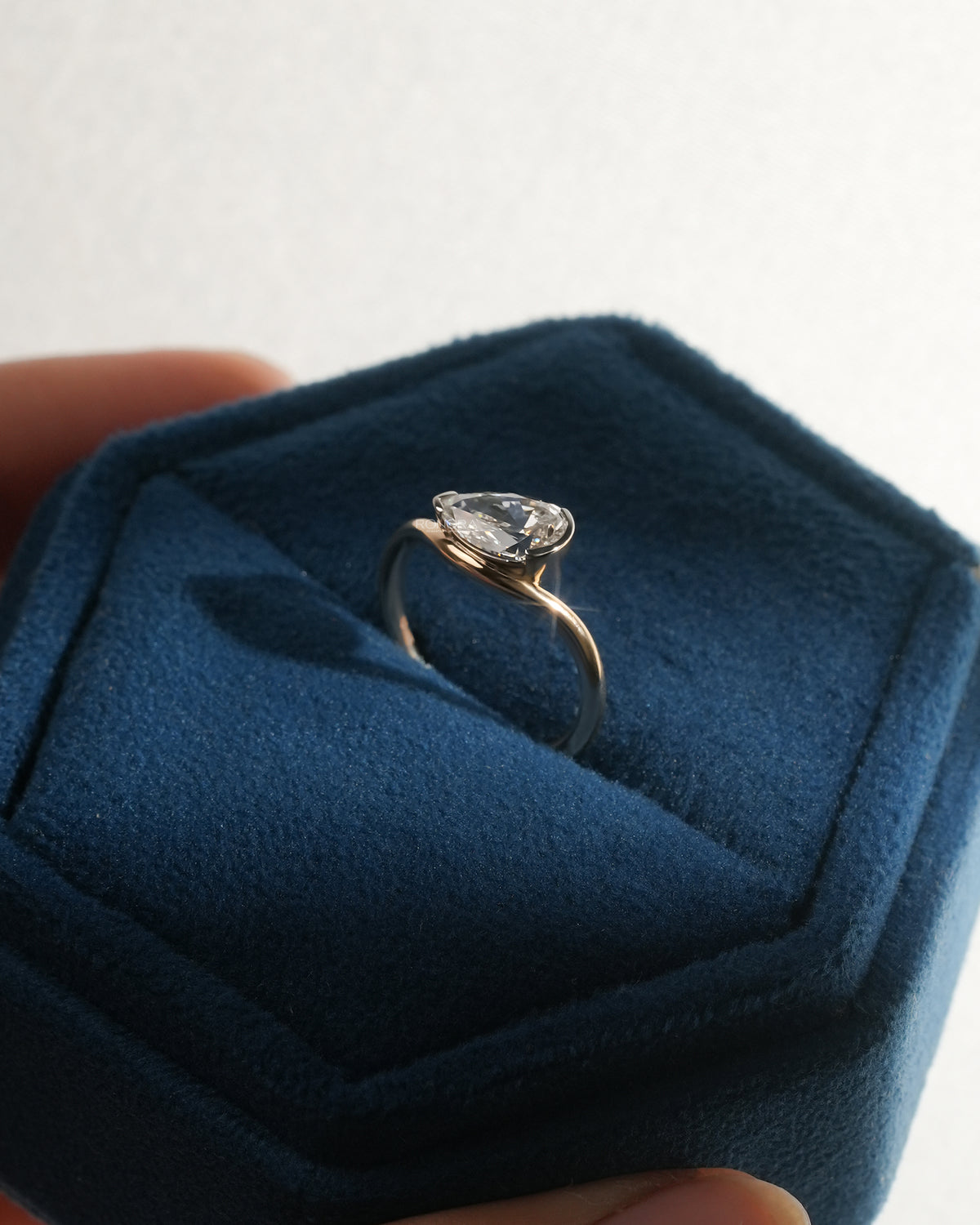 Angled view of an east west pear lab grown diamond ring in an open blue velvet ring box held between fingers