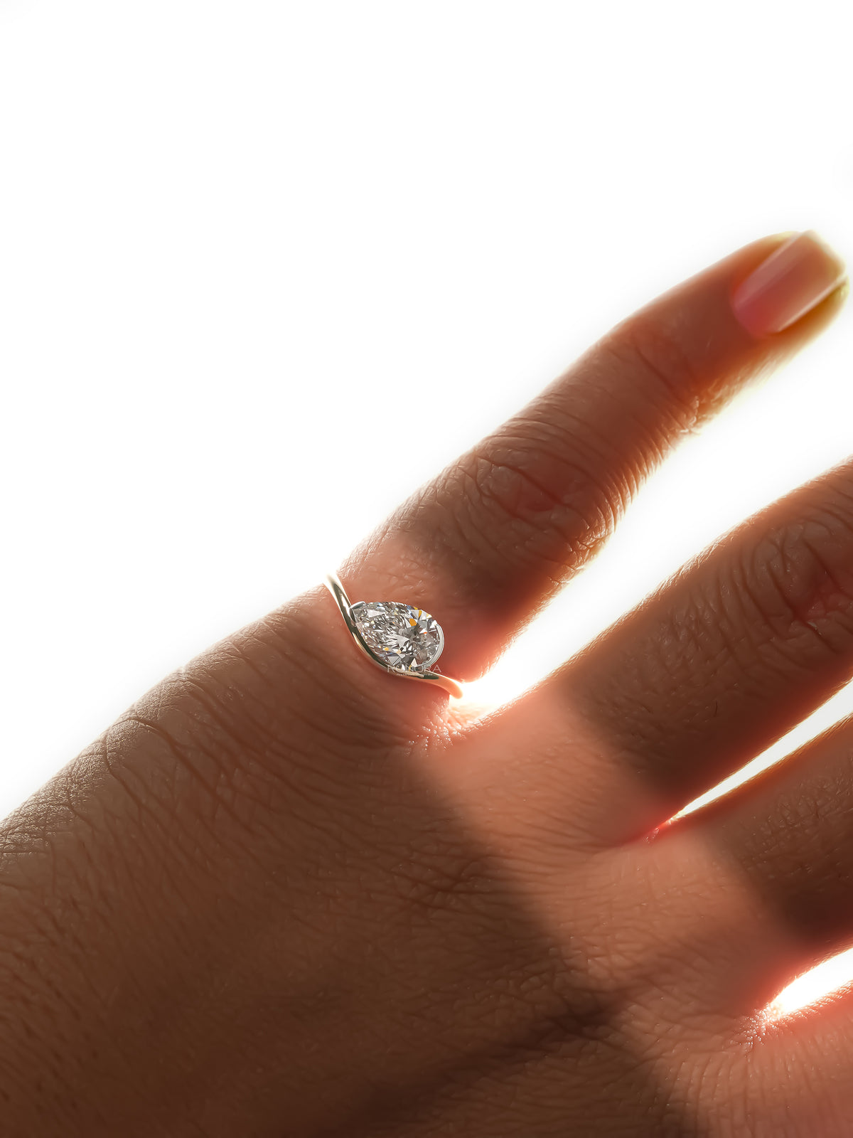 East west pear lab grown diamond ring on a hand in strong backlight, gold band sweeping around the stone
