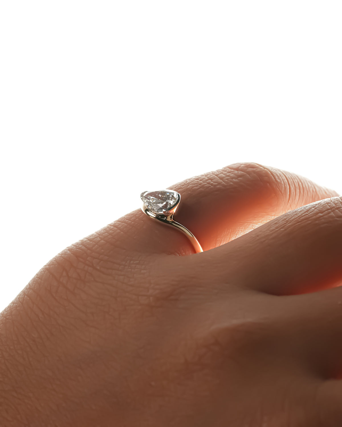 Side view of an east west pear lab grown diamond ring on a finger, showing the curved gold band and setting