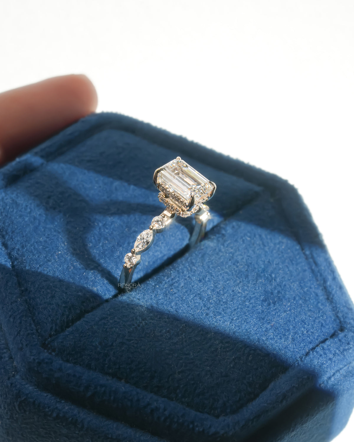Angled view of an emerald cut lab grown diamond ring with marquise side diamonds, resting in a blue velvet ring box