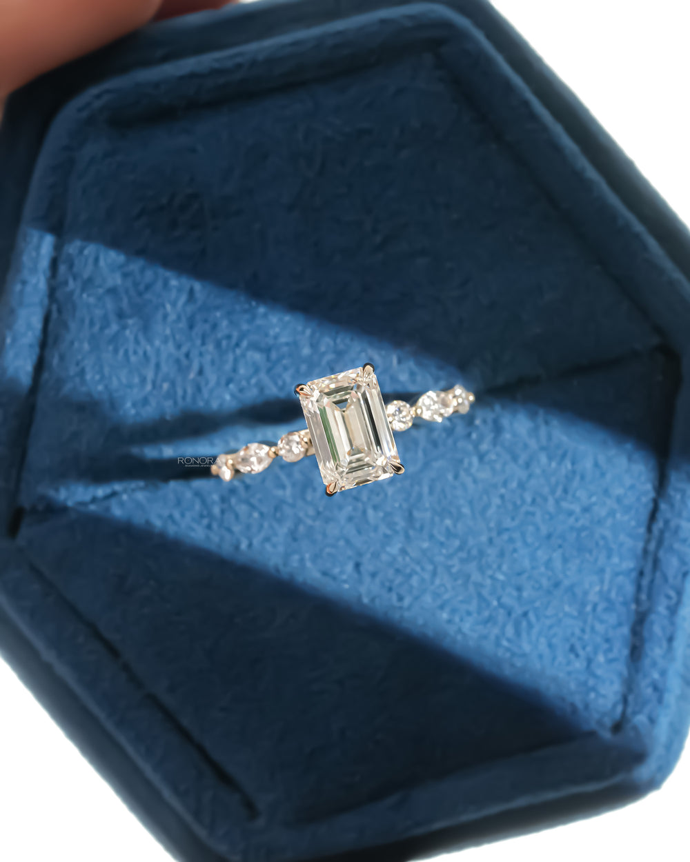 Top view of an emerald cut lab grown diamond ring with marquise and round side diamonds in a blue velvet ring box
